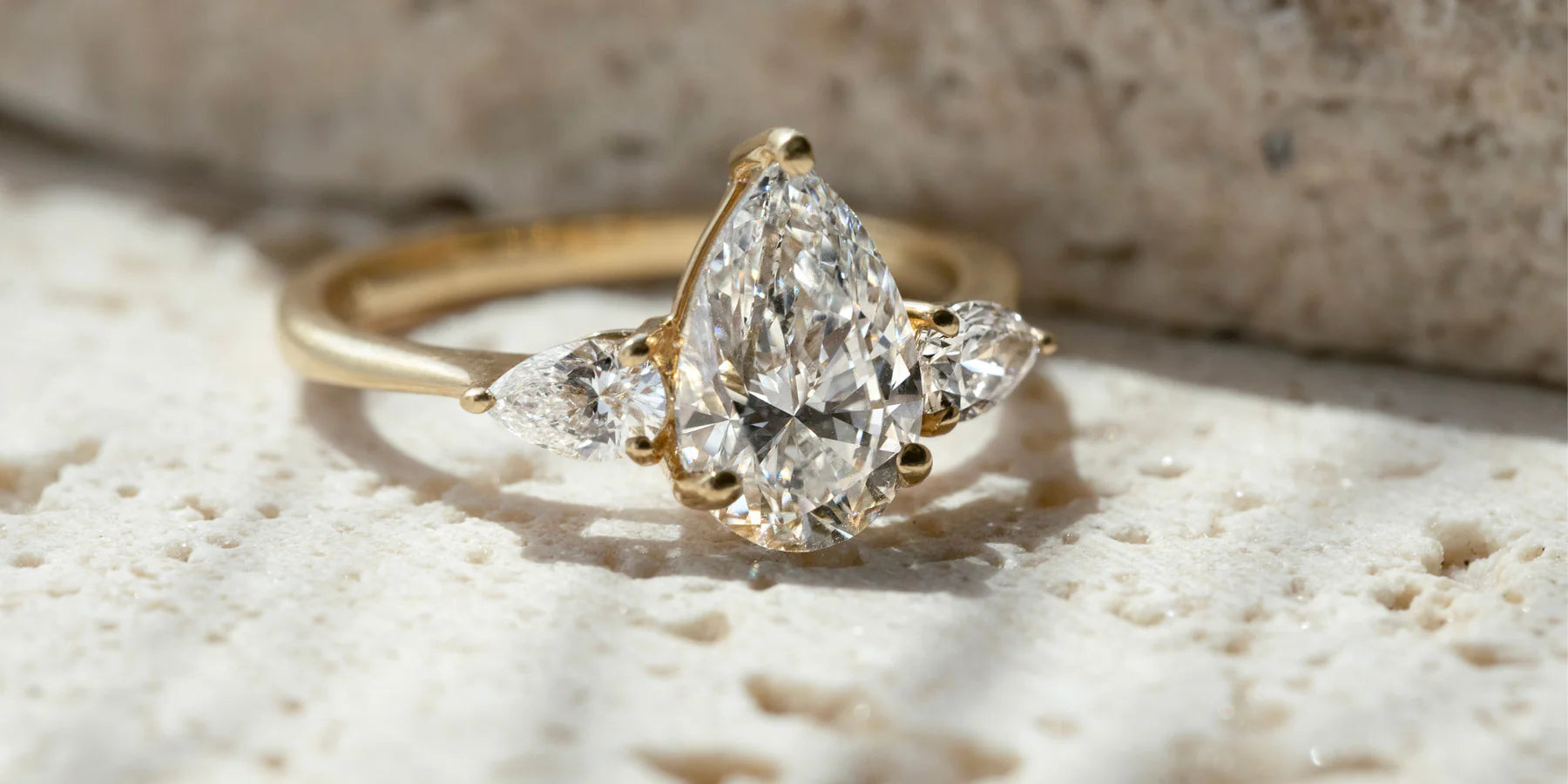 Saint Stones model showcasing a gold ring with a pear-shaped diamond on a textured surface, styled for luxury bridal jewelry photography in Colorado
