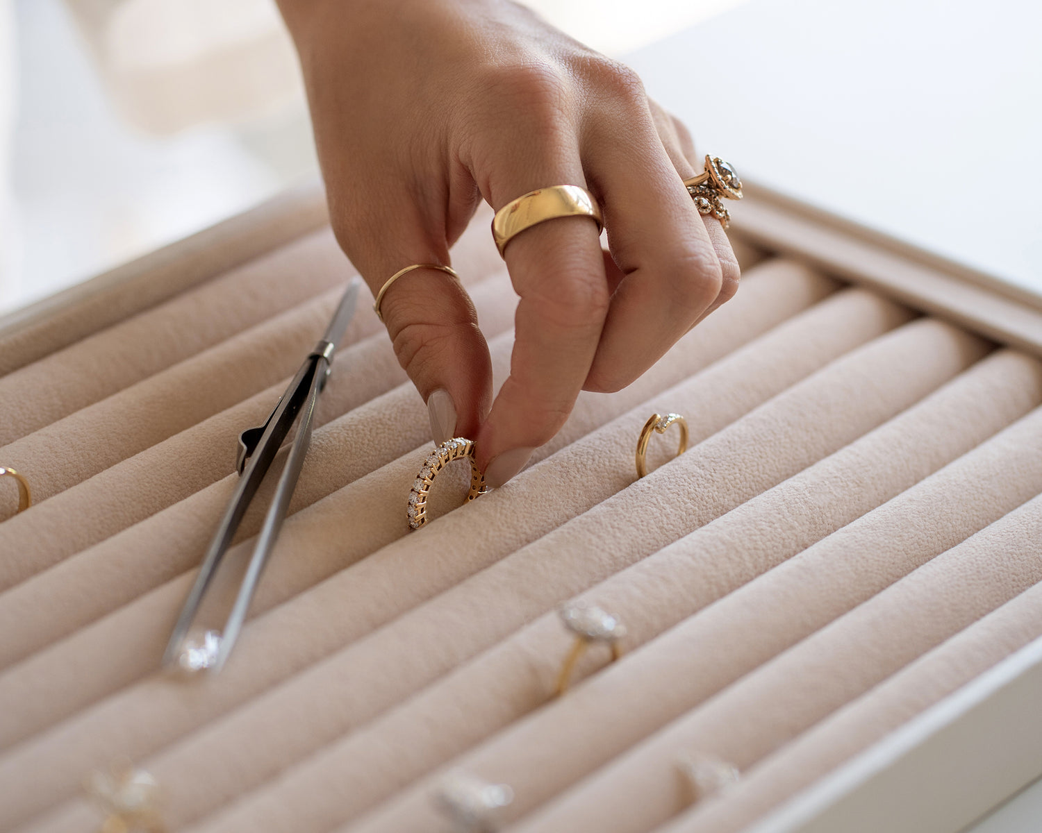 Saint Stones founder Ashlynne arranging gold rings on a beige jewelry display using tweezers, styled for luxury bridal jewelry photography in Colorado