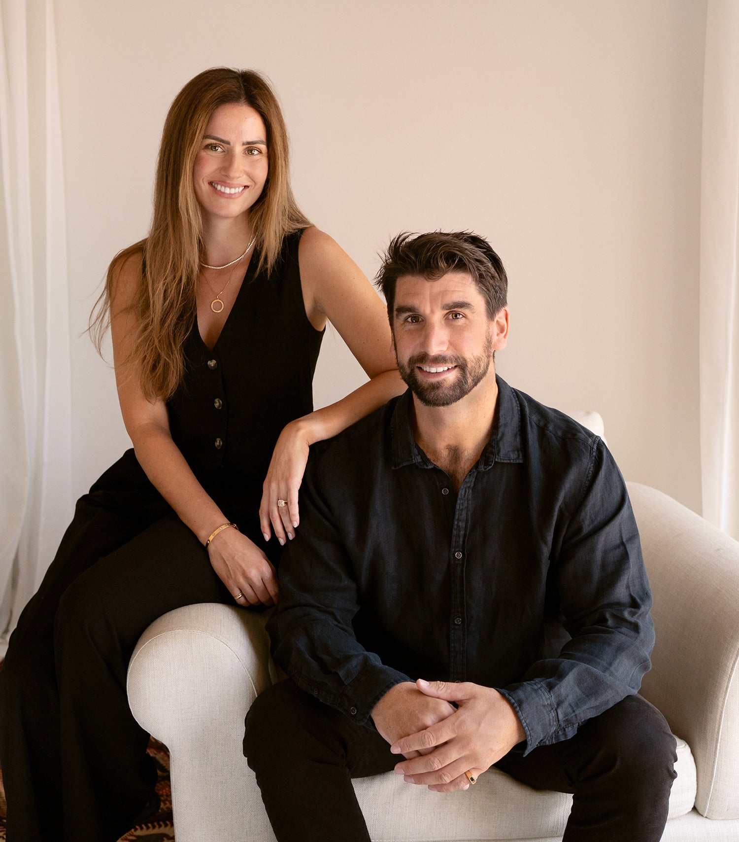 Saint Stones founders Ben and Ashlynne sitting together on a white couch in a neutral-colored room, styled for luxury jewelry branding photography in Colorado