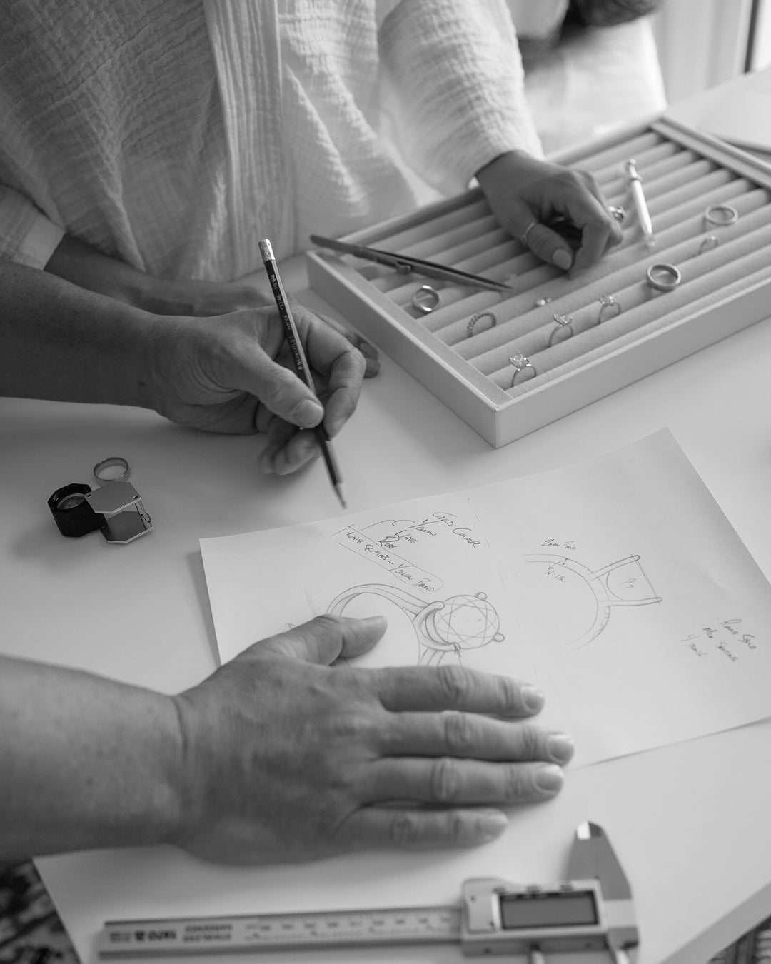 Saint Stones founders Ashlynne and Ben working on jewelry design with sketches and tools on a table, styled for luxury bridal jewelry creation in Colorado